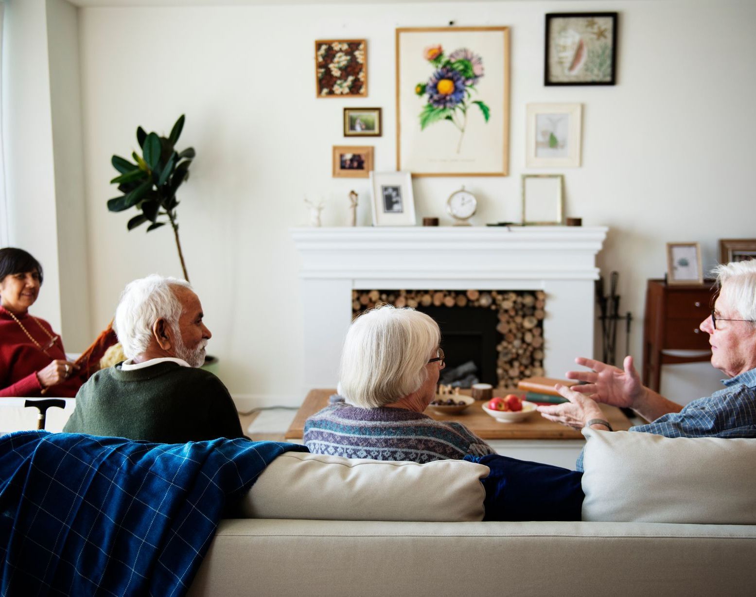 People seated in a cozy living room, chatting near a white fireplace with framed art above it