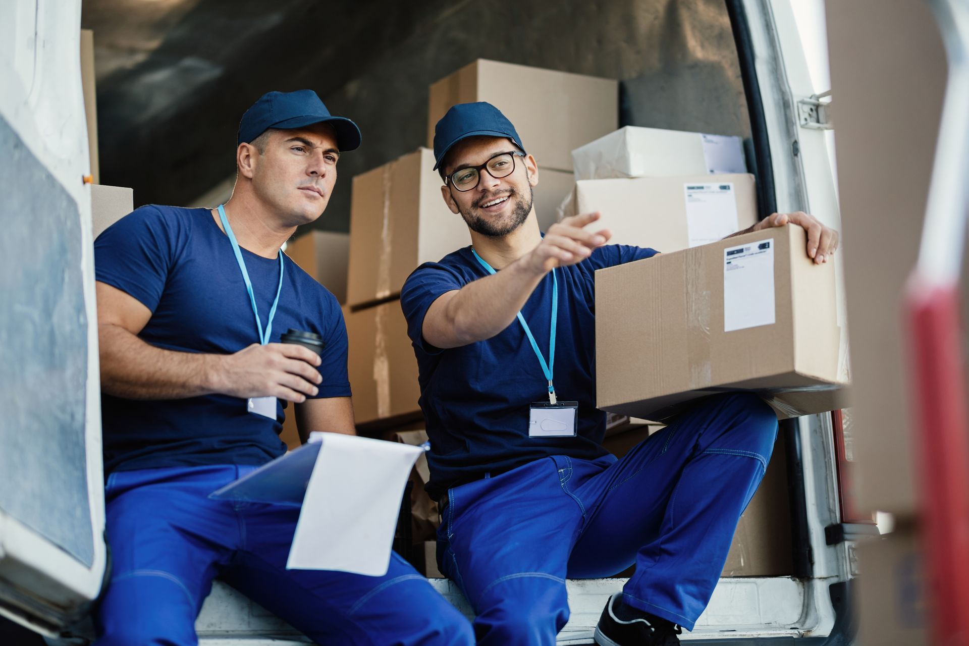 Two movers in blue uniforms loading boxes into a truck and discussing where to place them