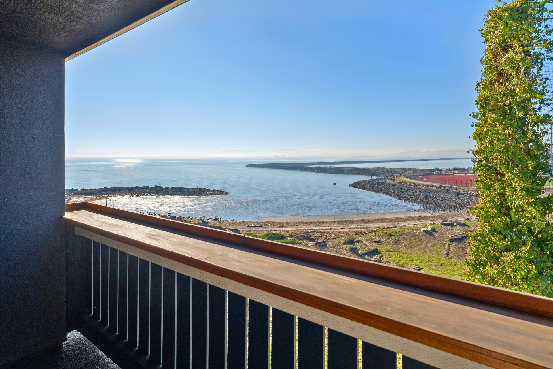 Balcony view of a calm bay and coastline under a clear blue sky at Ballena Village apartments in Alameda, CA.