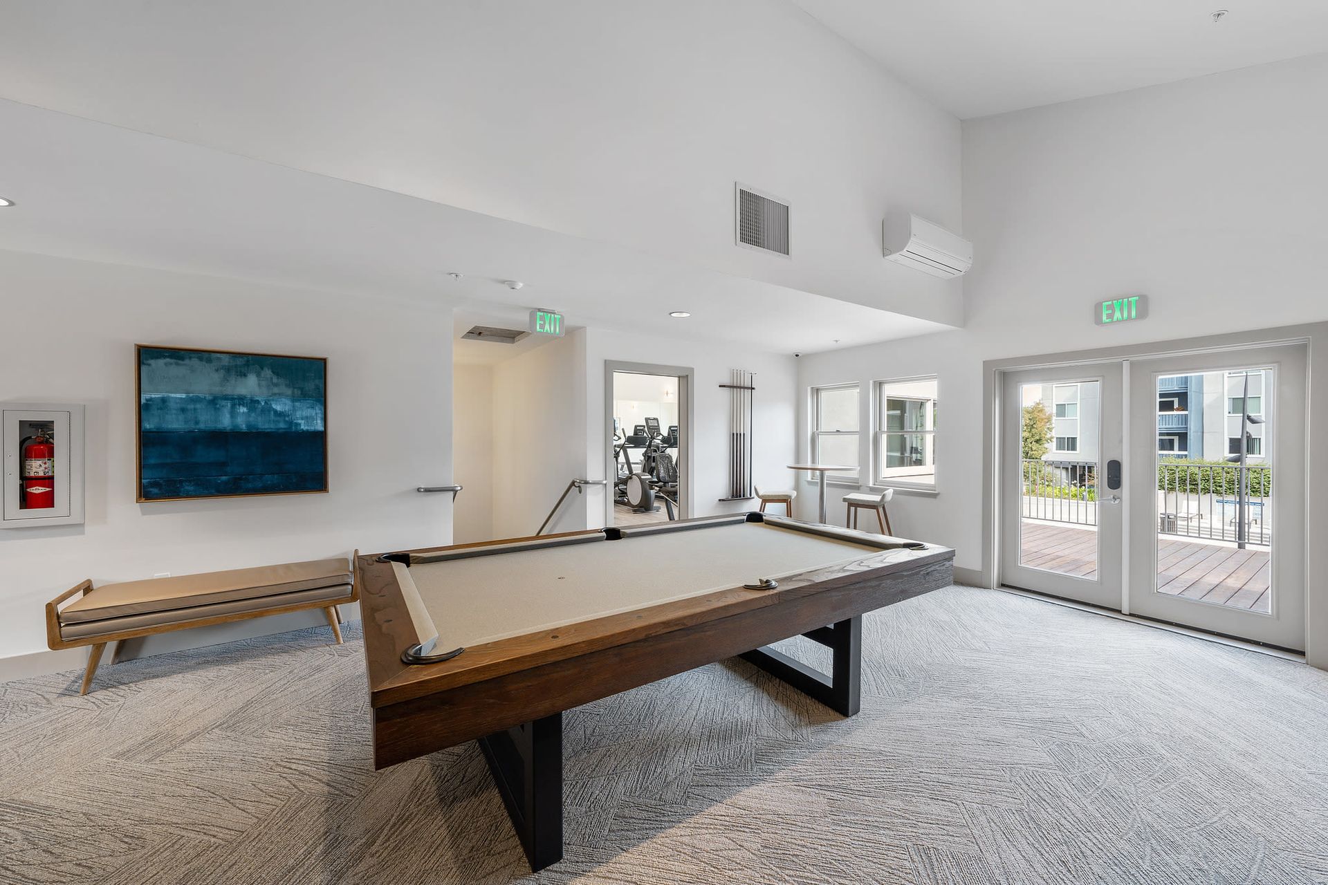 Indoor community recreation room with a billiards table, bench seating, and exit doors at Ballena Village apartments in Alameda, CA.