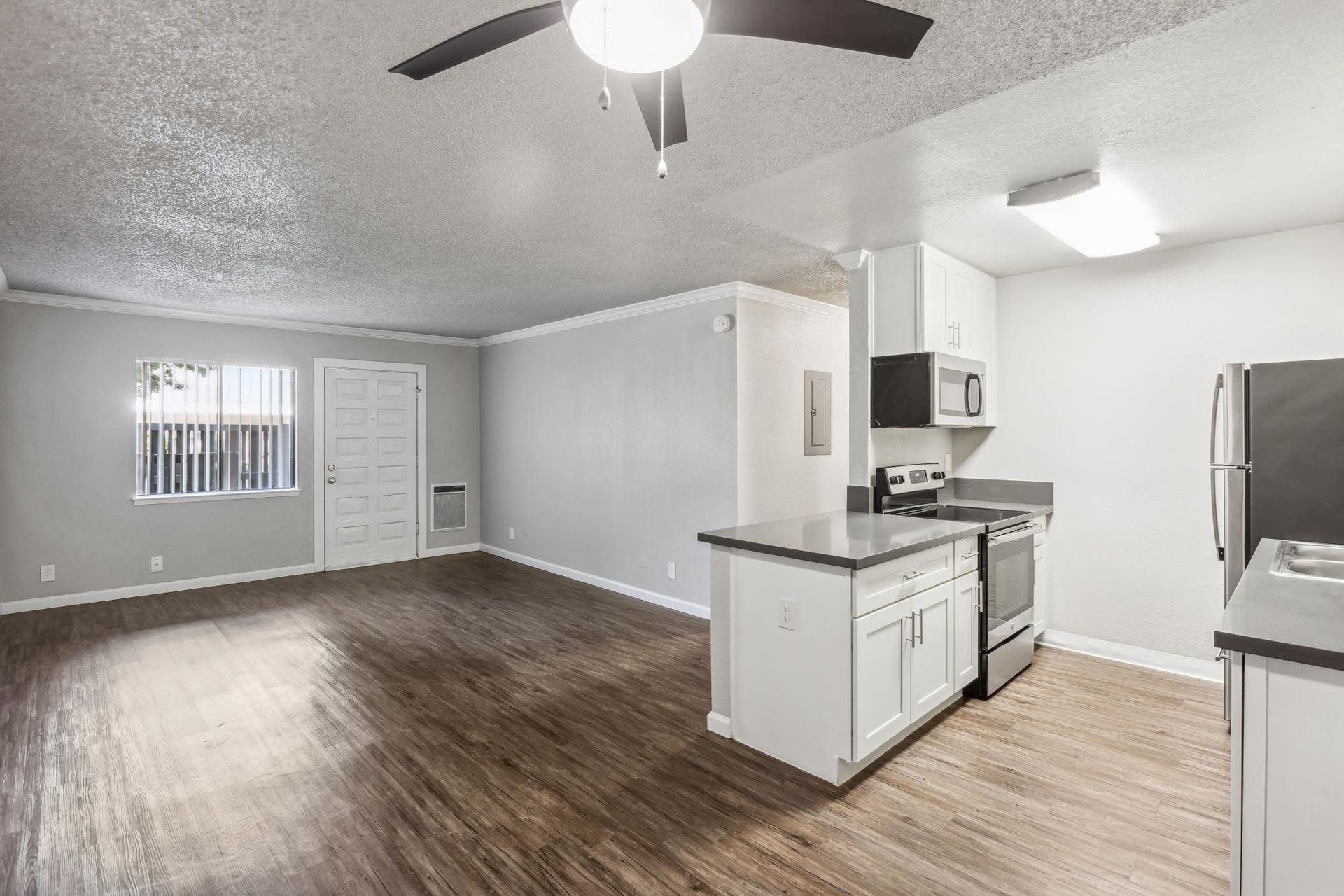 Open-concept living area with a kitchen, white cabinets, stainless steel appliances, wood-look flooring, and a ceiling fan at Ballena Village apartments in Alameda, CA.