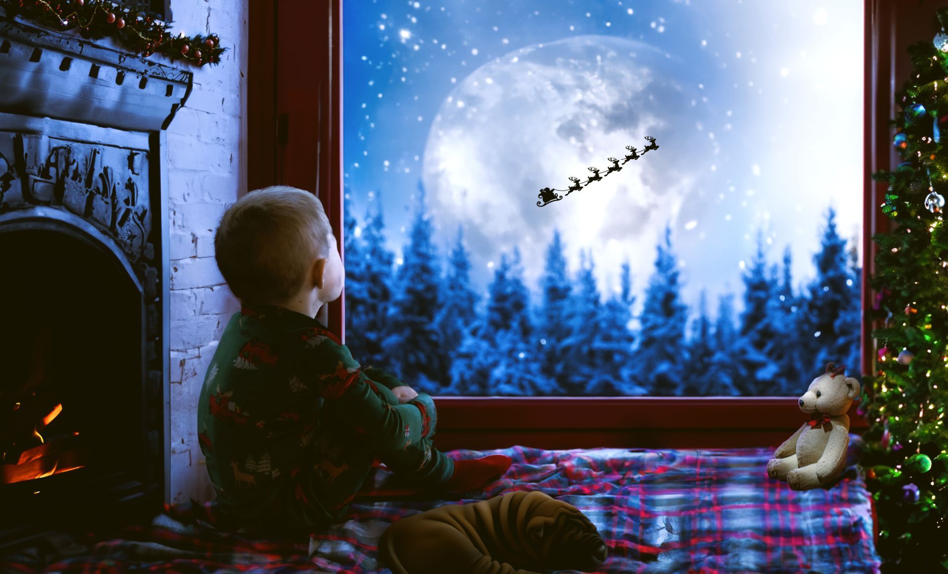 A little boy is sitting in front of a window looking out at santa claus flying in the sky.