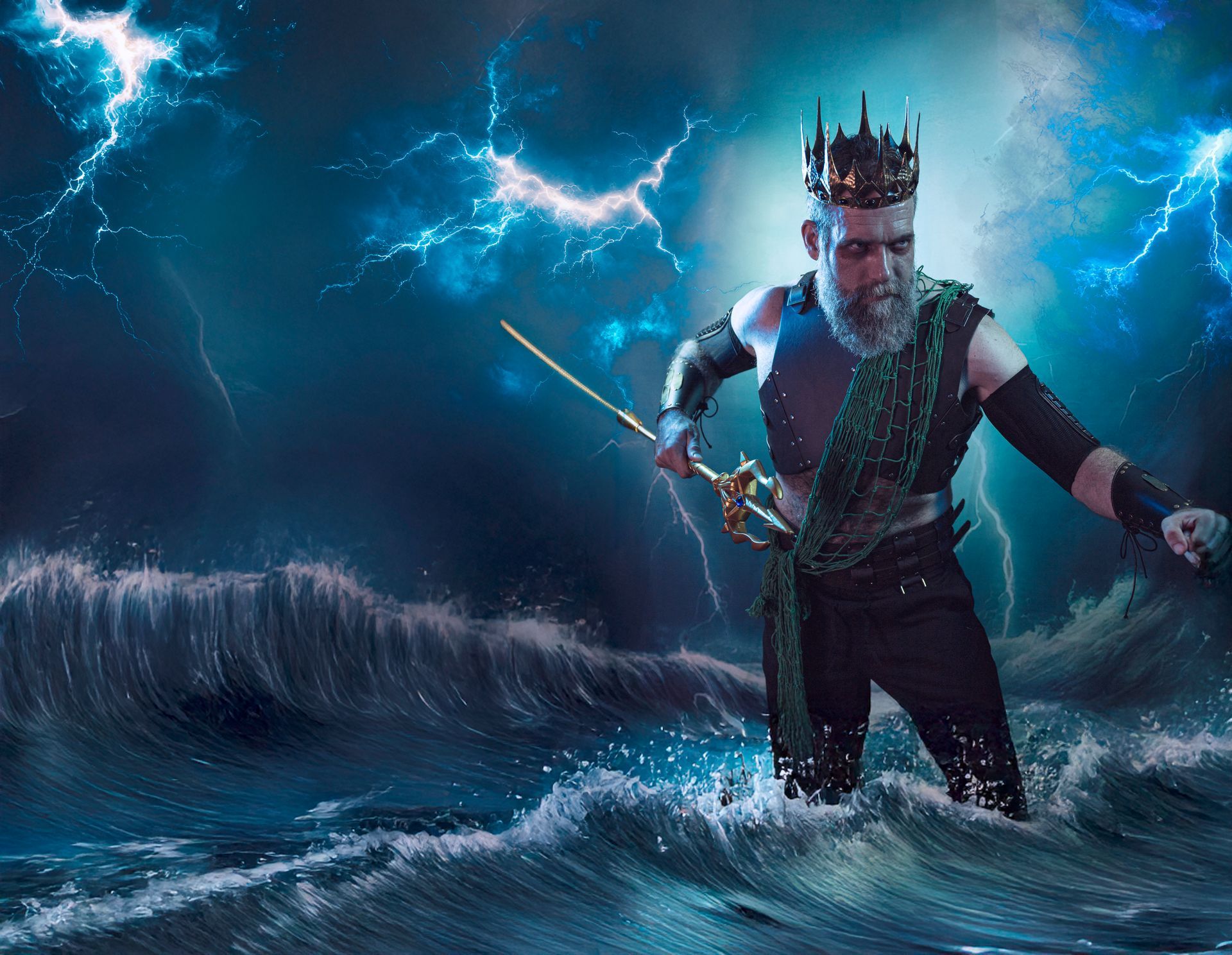 Man dressed as Poseidon, wading in ocean with crown and trident, stormy sky in background.