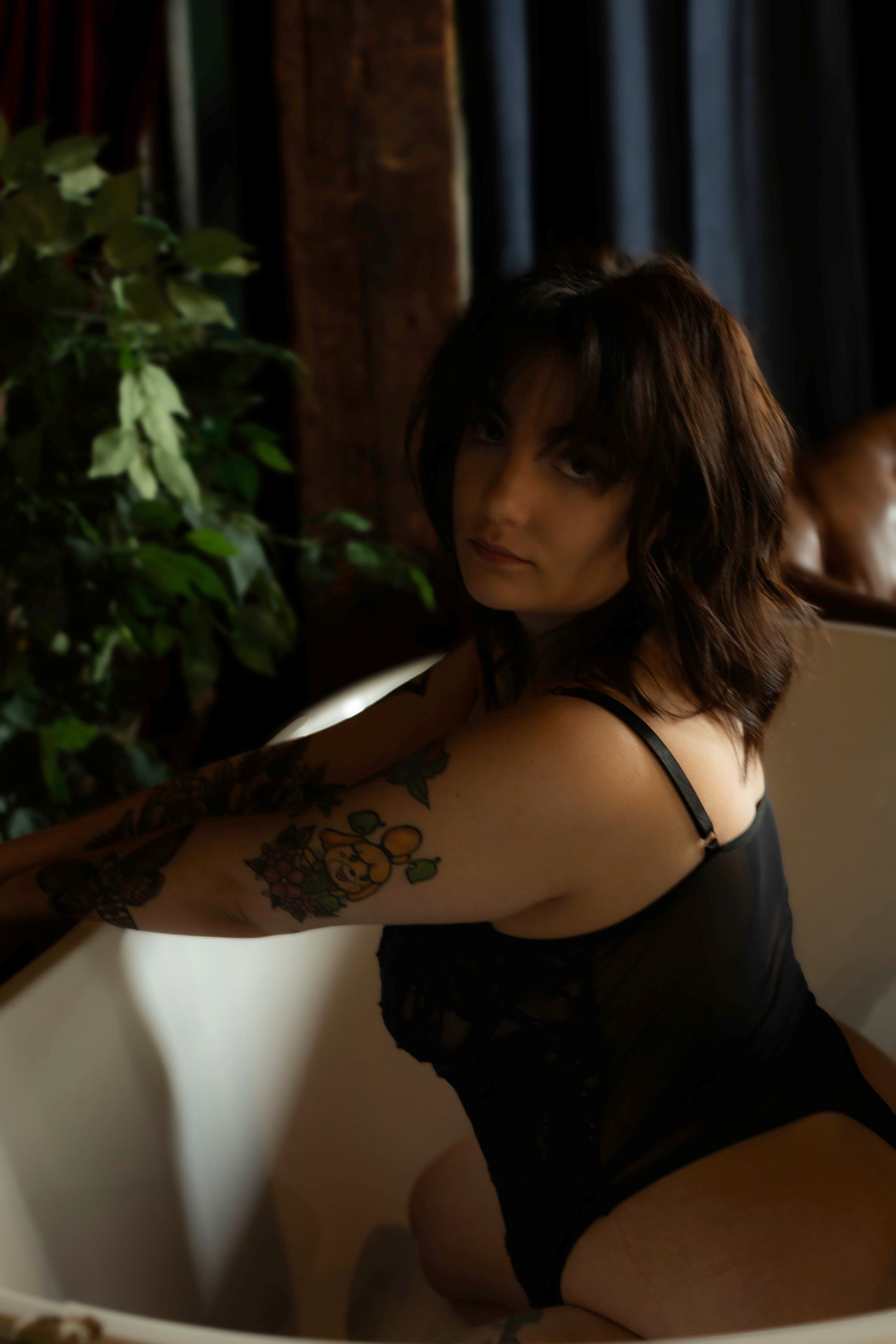 A woman in a black bodysuit is sitting in a bathtub.
