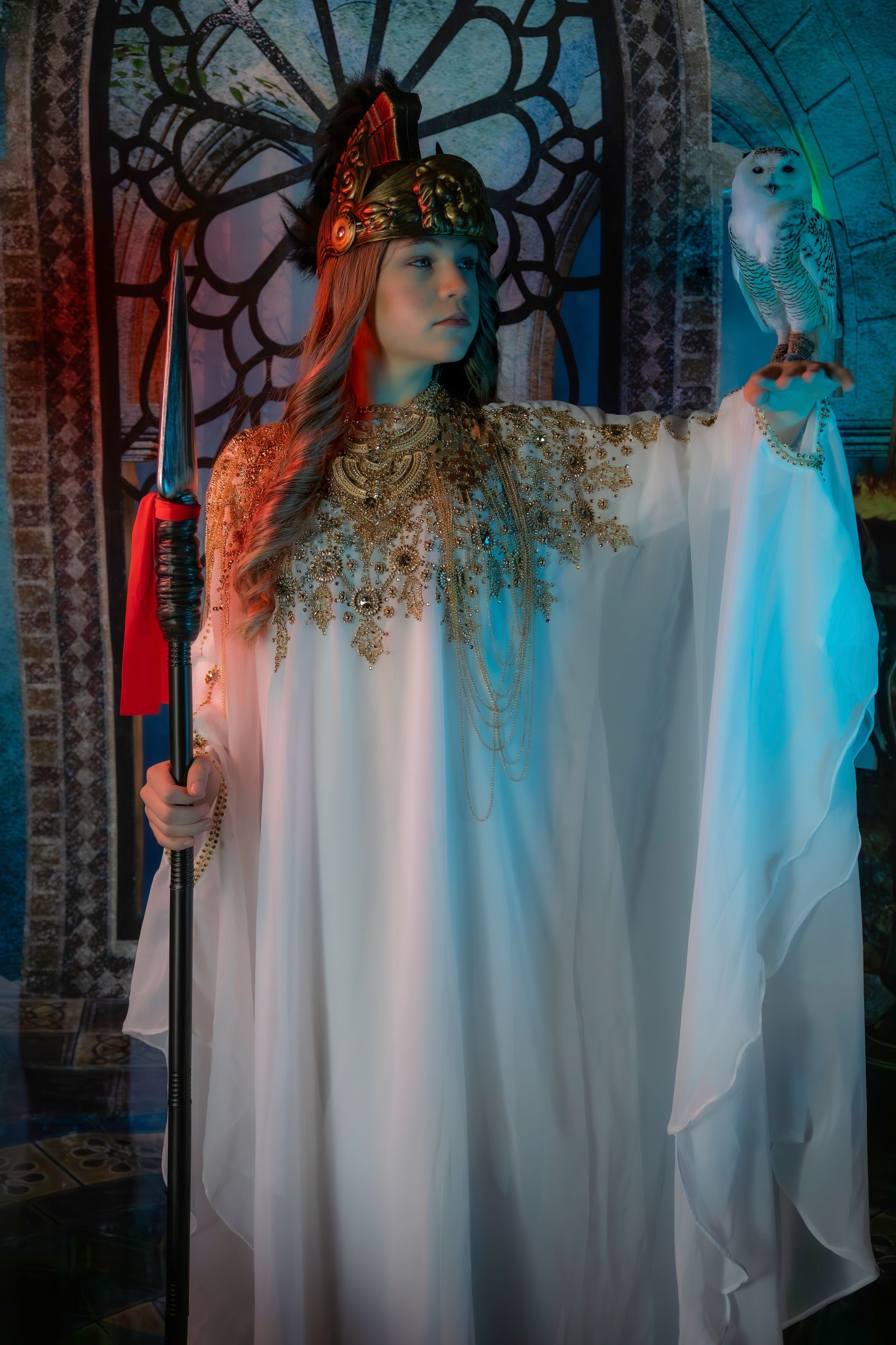 Woman in white and gold gown, holding a spear and an owl in an ornate setting.