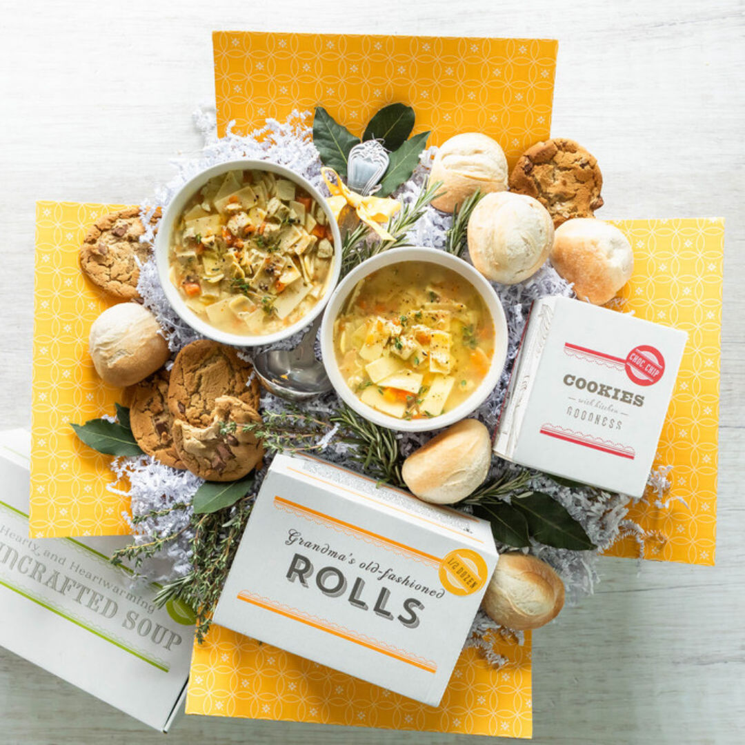 A box of rolls is surrounded by bowls of soup and cookies