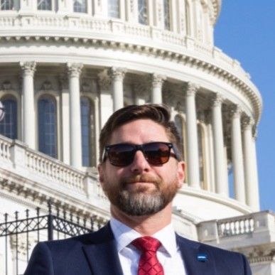 A man in a suit and tie is standing in front of the capitol building.