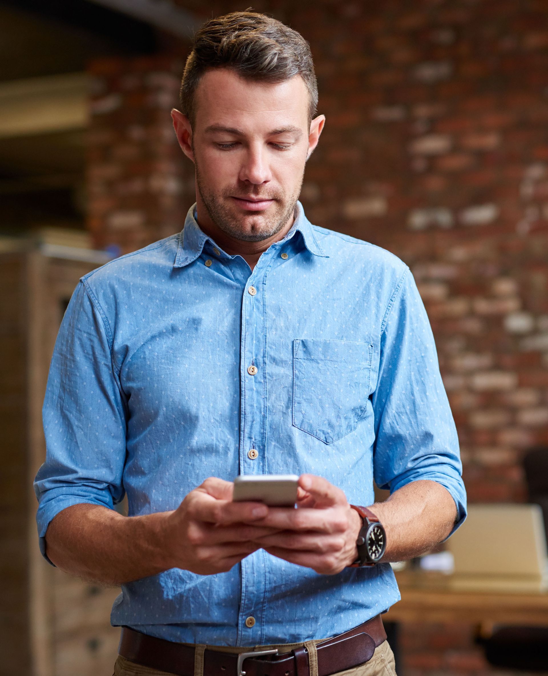 A man in a blue shirt is looking at his cell phone.
