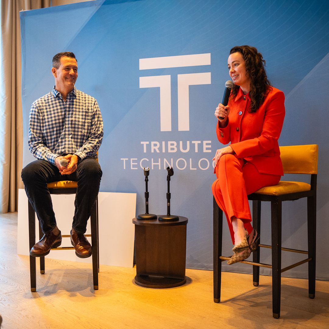 A man and a woman are sitting in front of a sign that says tribute technology