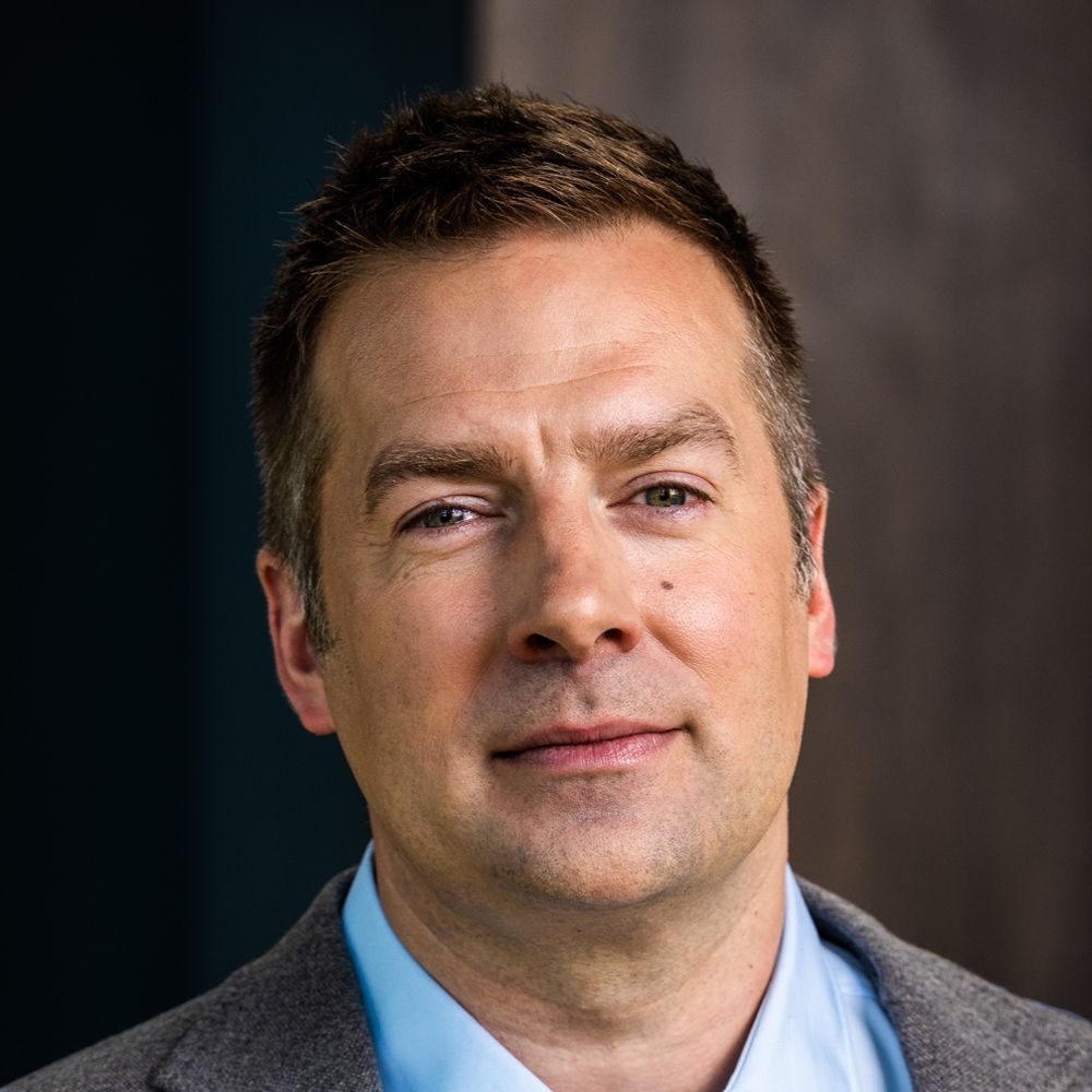 A man in a suit and blue shirt is looking at the camera.