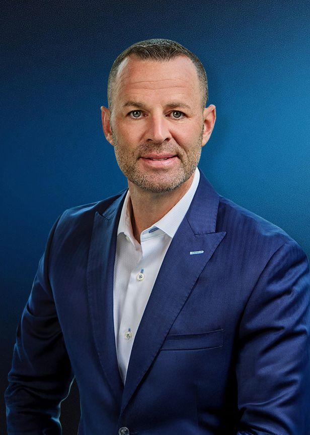 A man in a blue suit and white shirt is standing in front of a blue background.