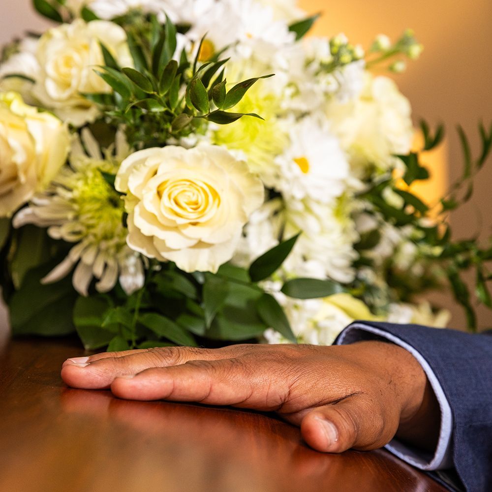 A person 's hand rests on a table in front of a bouquet of flowers