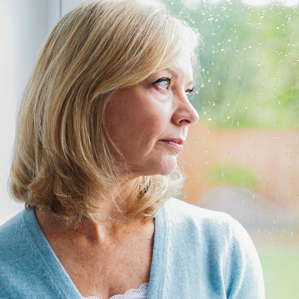 A woman in a blue sweater is looking out of a window.