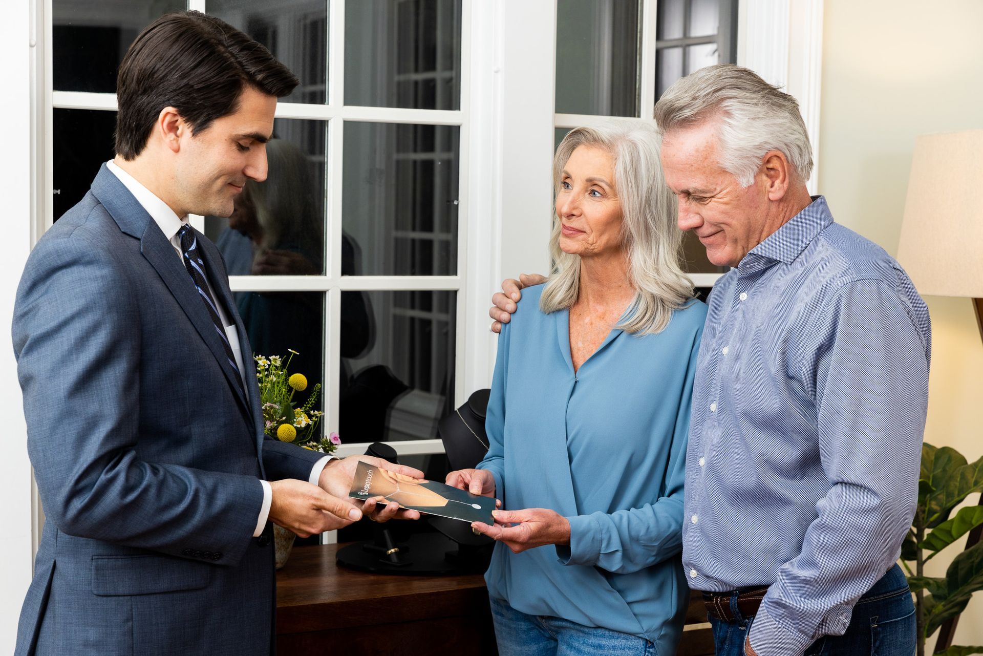 A man in a suit and tie is talking to a man and woman in a living room.