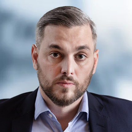 A man with a beard is wearing a suit and a blue shirt.