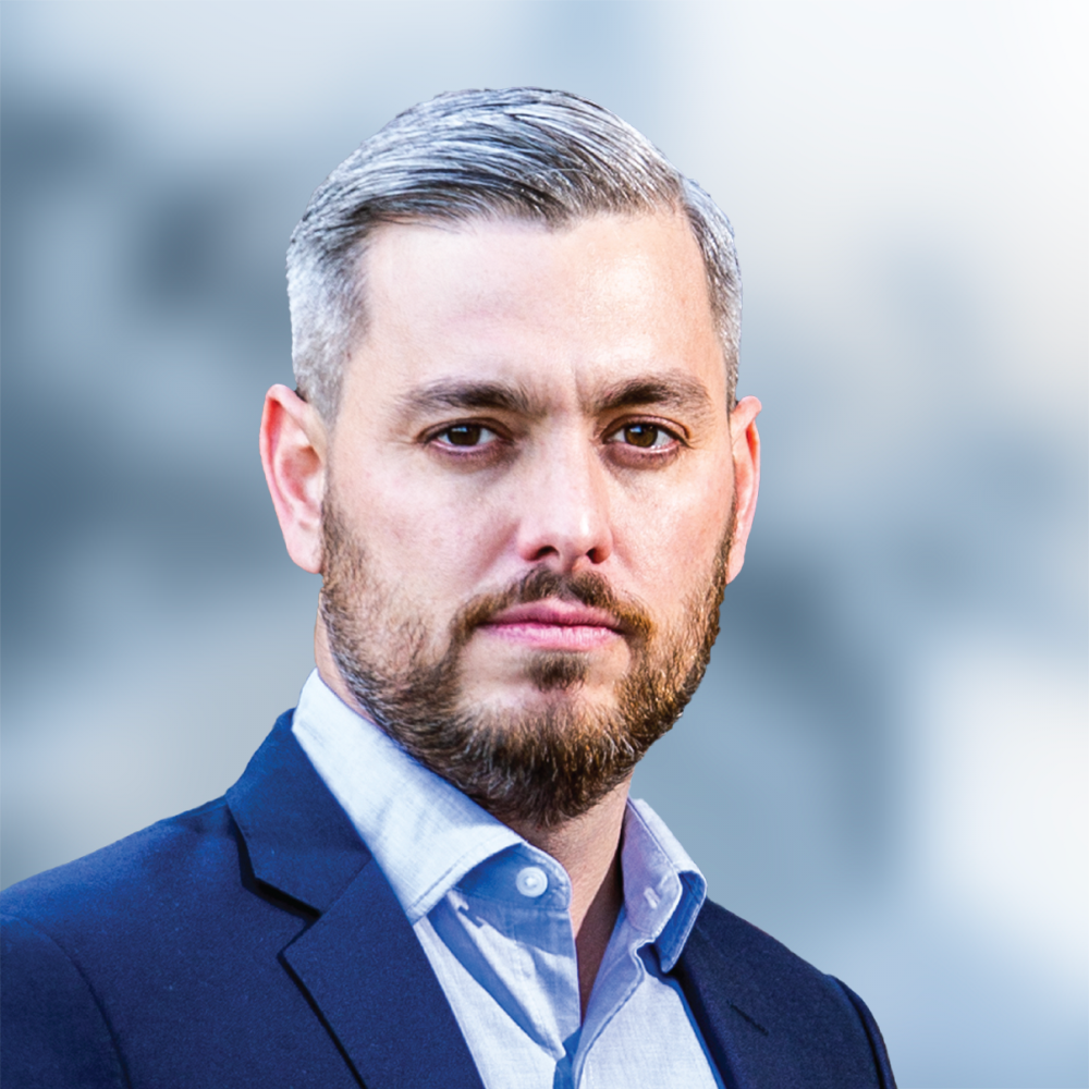 A man with a beard is wearing a suit and looking at the camera.
