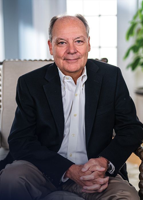 A man in a suit is sitting in a chair with his hands folded.