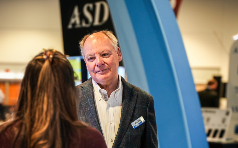 A man in a suit is talking to a woman in front of a sign that says asd.