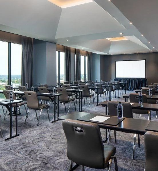 A large room with tables and chairs and a large screen.
