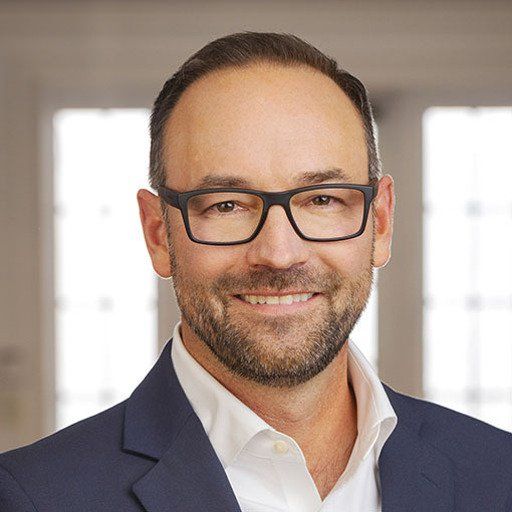 A man wearing glasses and a suit is smiling for the camera.