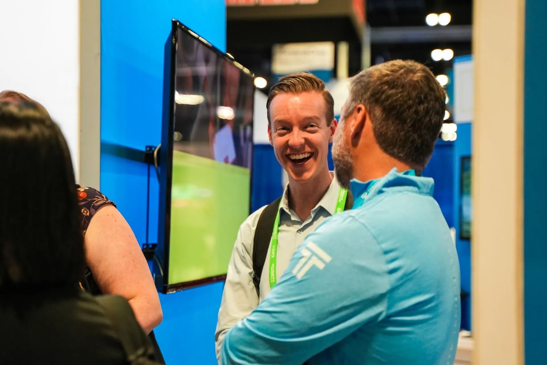 A group of people are standing around a table talking to a man in a blue shirt.