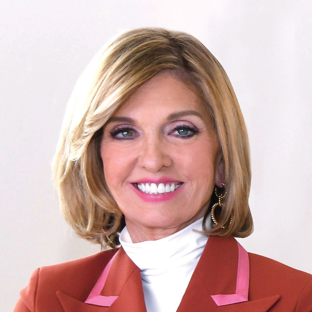 A woman wearing a brown jacket with a pink collar smiles for the camera