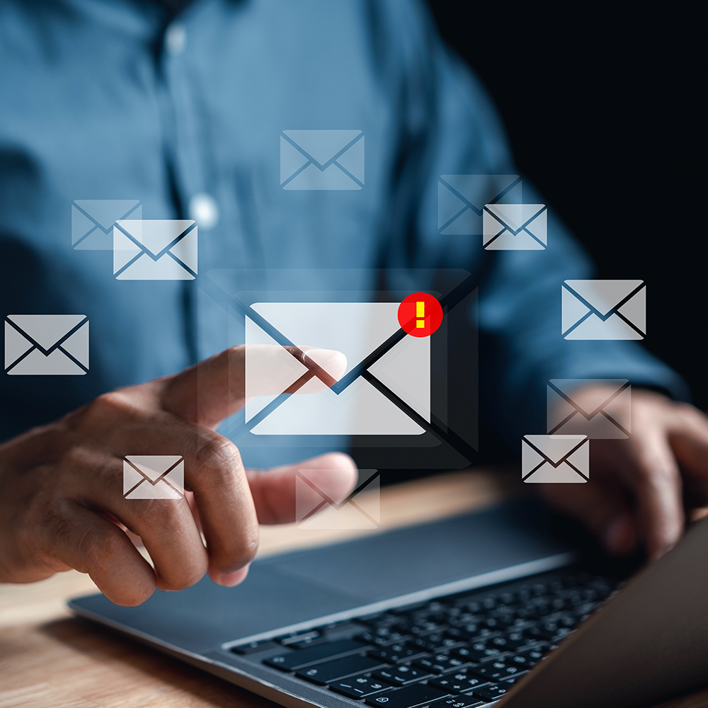 A man is typing on a laptop computer with envelope icons coming out of it.