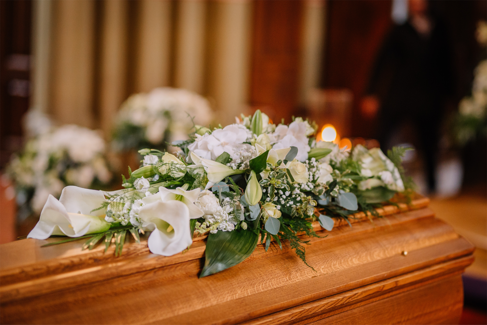 A man in a suit is sitting at a coffin at a funeral.