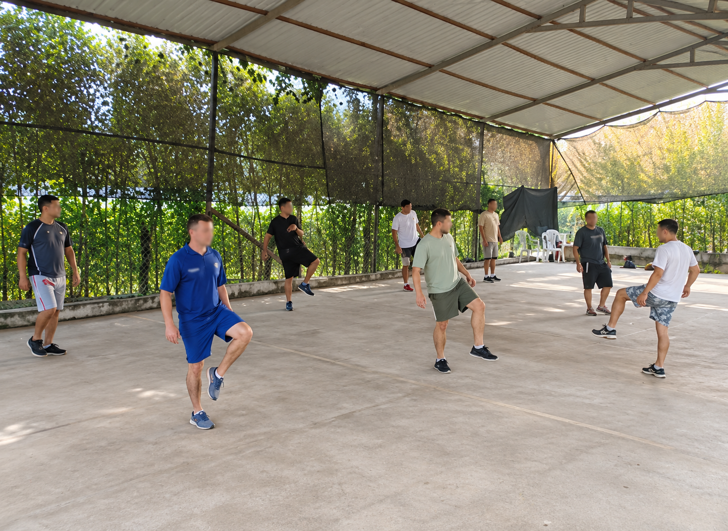 Personas haciendo ejercicio en una pista exterior cubierta, elevando las rodillas al unísono en una sesión de entrenamiento grupal.