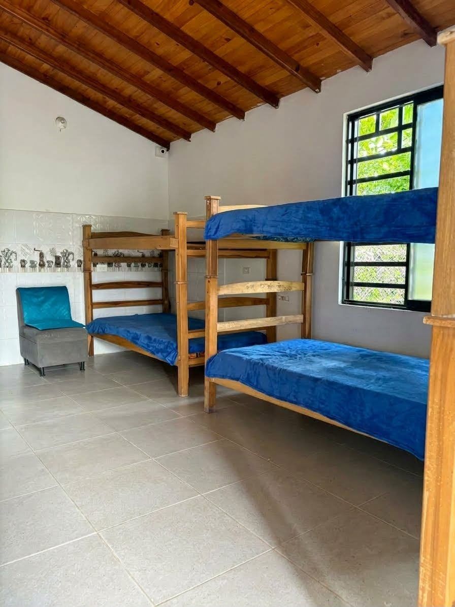 Habitación compartida con literas azules, paredes blancas, suelo de baldosas y una ventana por la que entra la luz del día