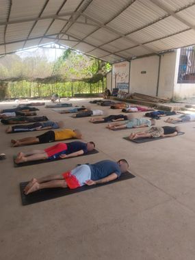 Personas tumbadas sobre esterillas en un pabellón cubierto y al aire libre, que parecen estar descansando o haciendo ejercicio.