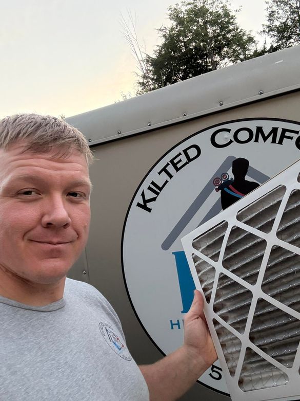 Man posing beside a Kilted Comfort sign with a white geometric object in front.