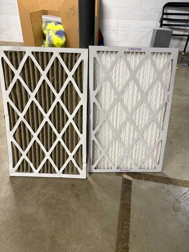 Two white accordion air filters leaning side by side on a concrete floor in a garage.
