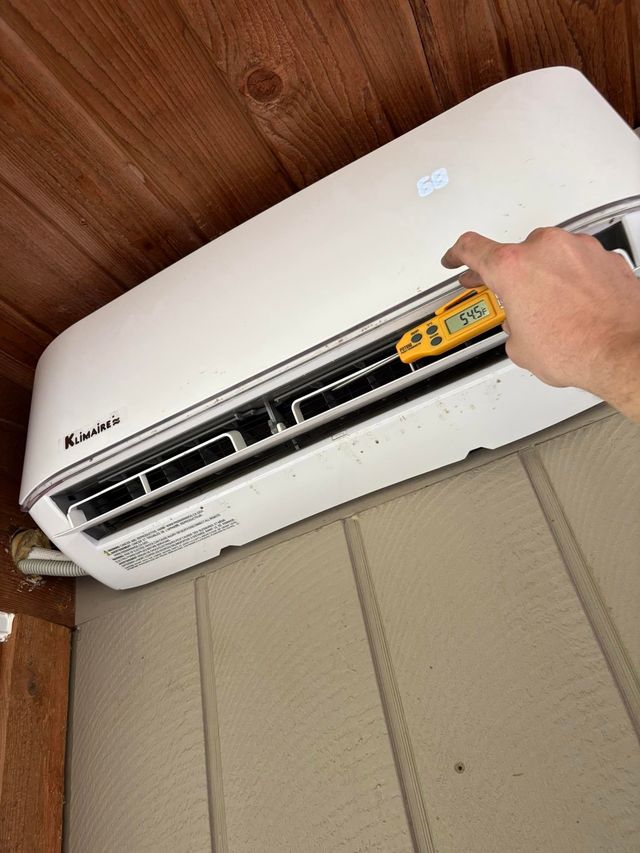 Hand turning a remote toward a white wall-mounted air conditioner in a room with wood ceiling