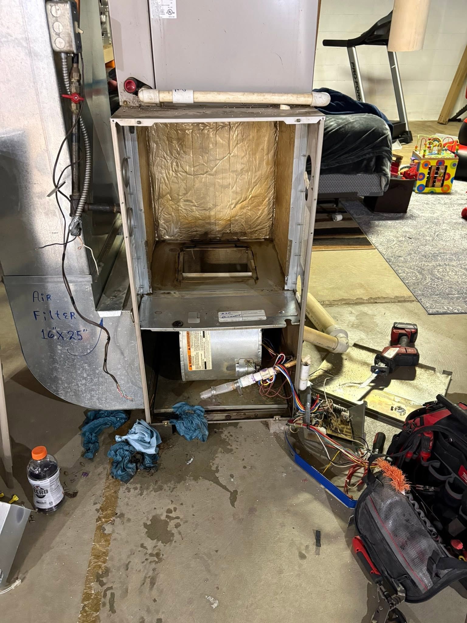 Open electrical panel with insulation and tools scattered on a concrete floor in a work area