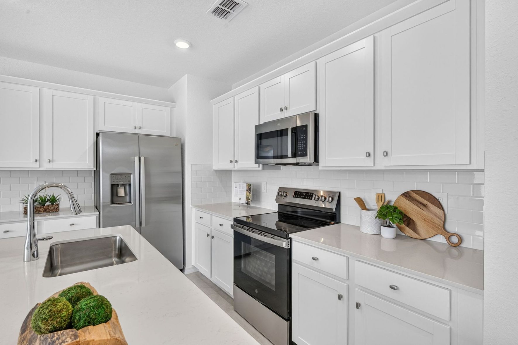 Bright white kitchen with stainless steel appliances, island sink, and wooden cutting boards on the counter