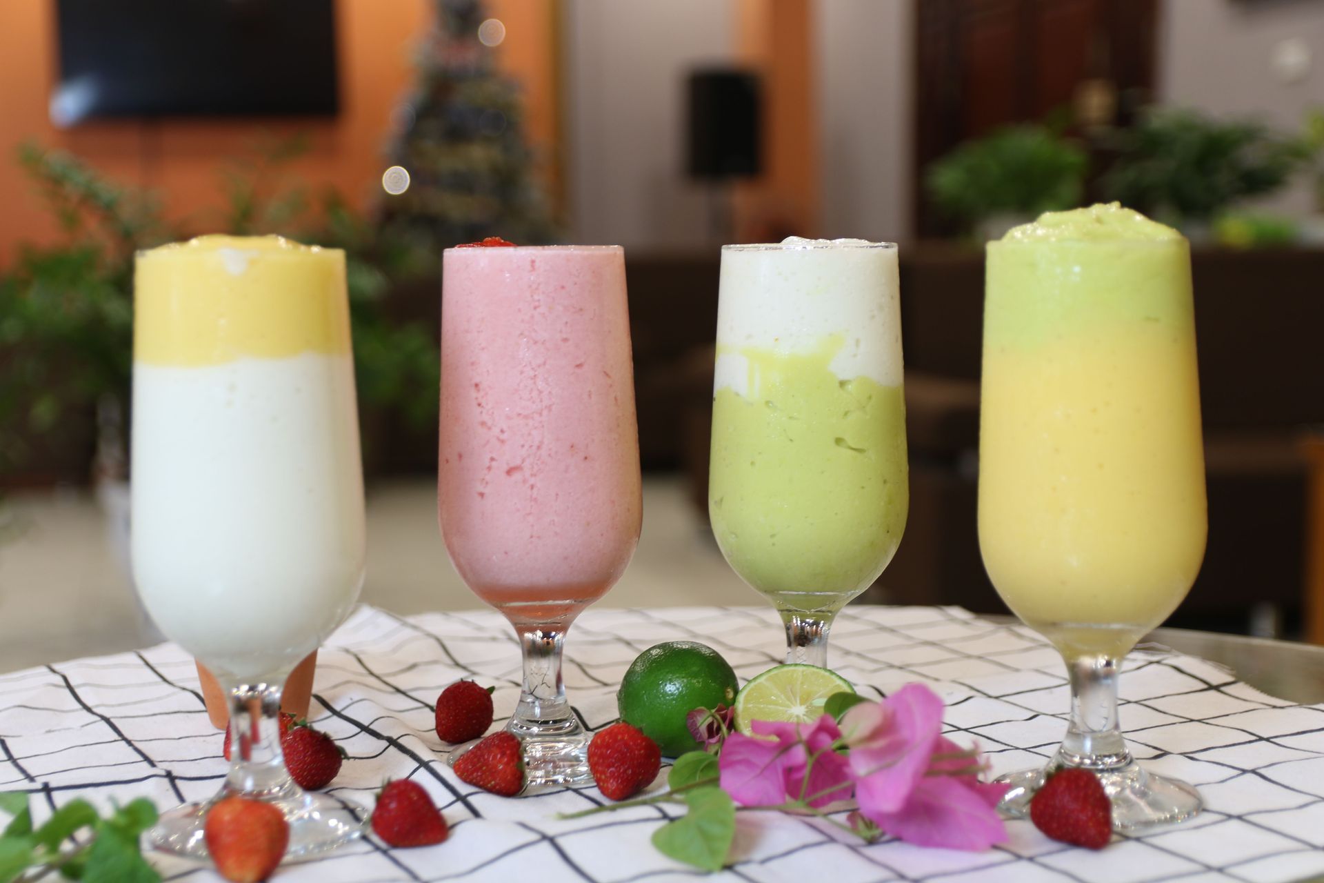 Four colorful layered drinks in flutes with strawberries and flowers on a tiled table outdoors