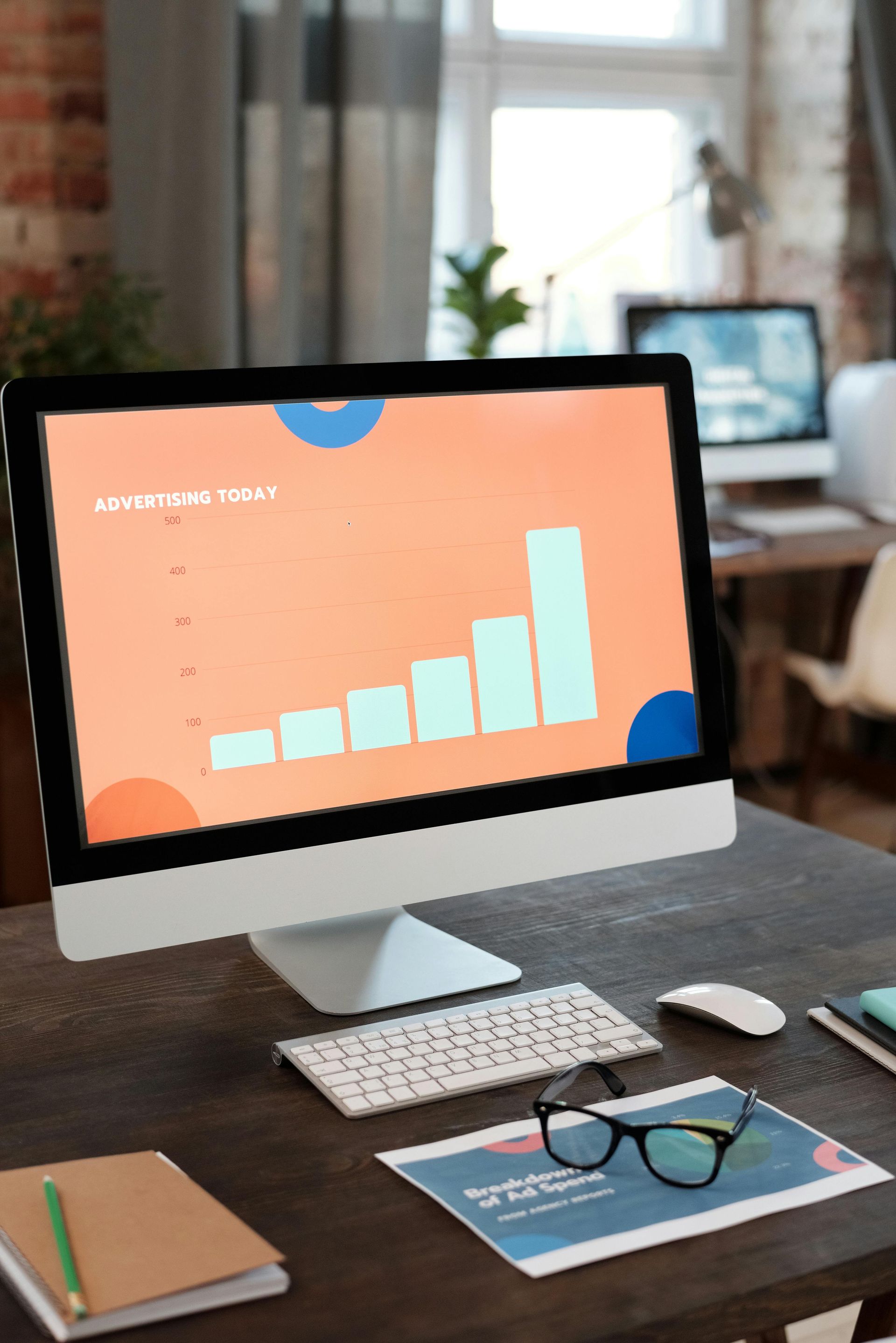 A computer monitor displays a bar graph on an office desk with glasses and documents.