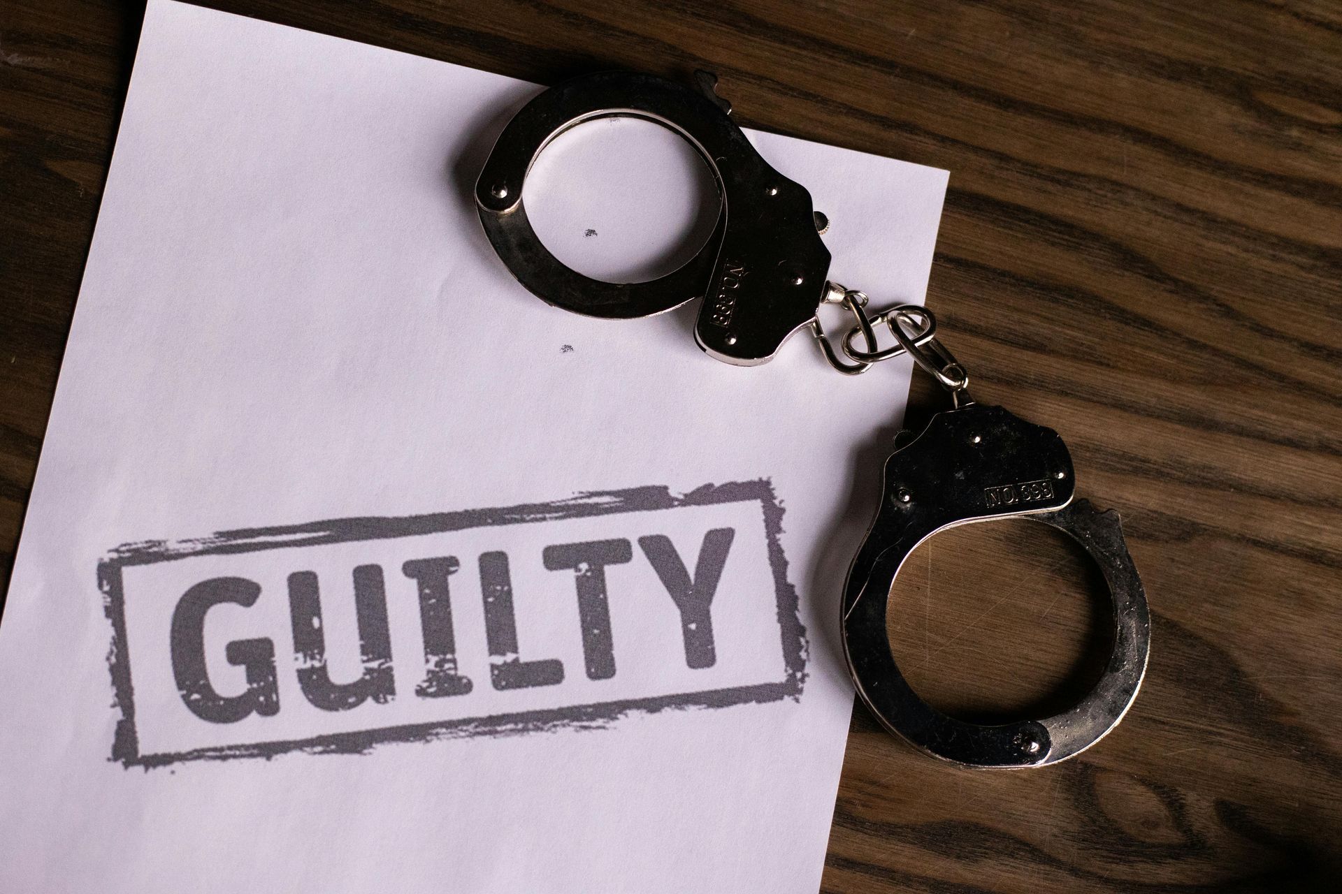 A pair of handcuffs next to a piece of paper that says guilty.