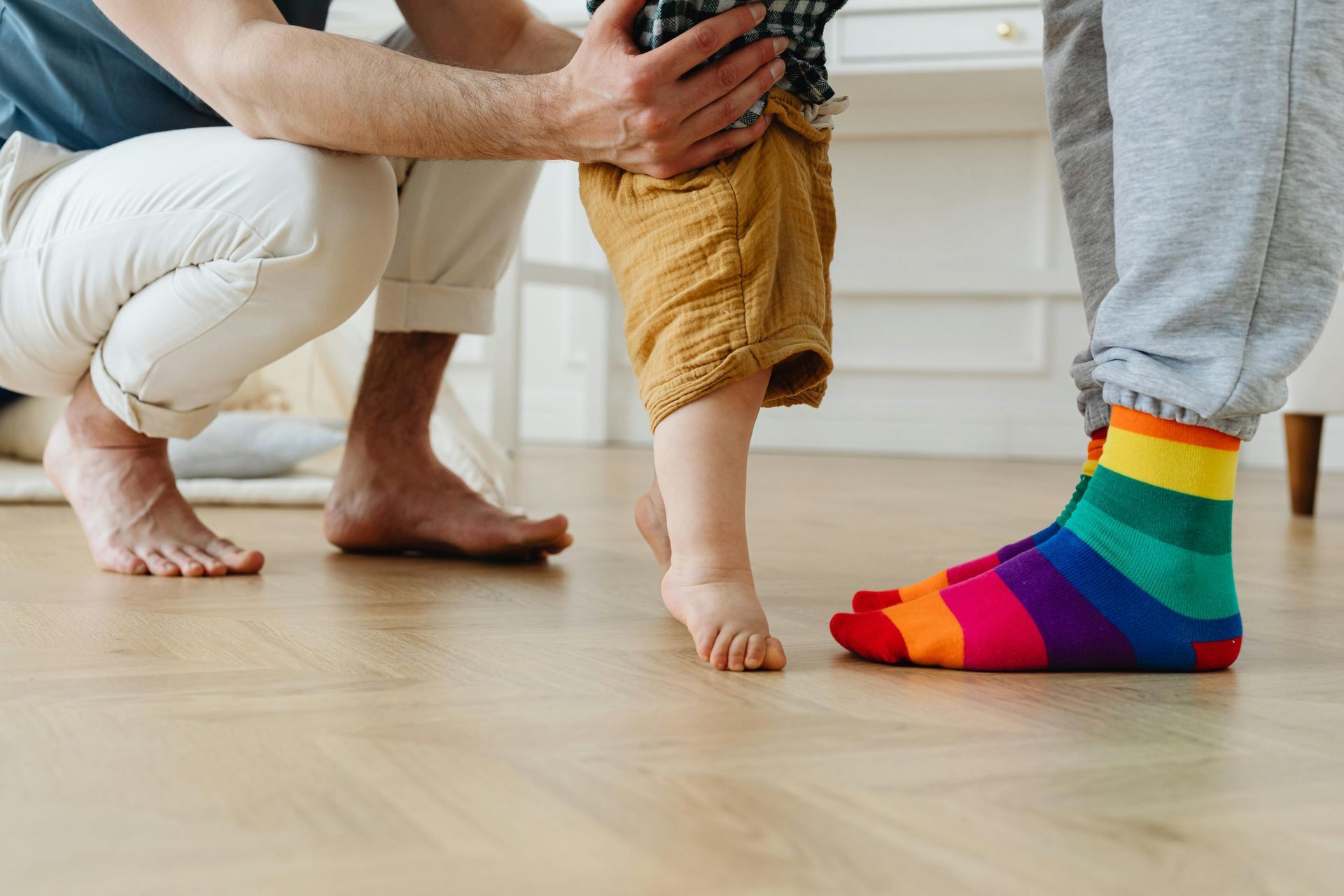 A man is kneeling down next to a baby wearing rainbow socks.