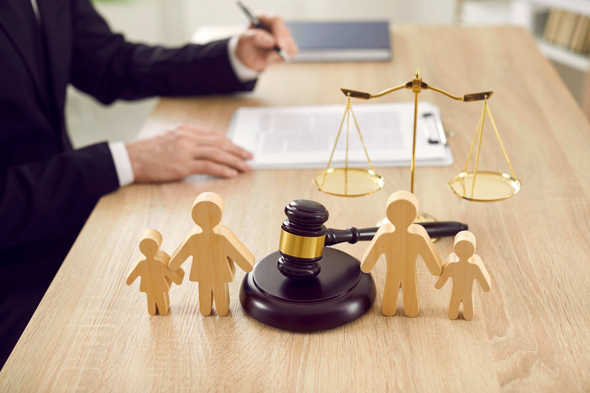 A judge is sitting at a table with a wooden family, scales of justice and a gavel.