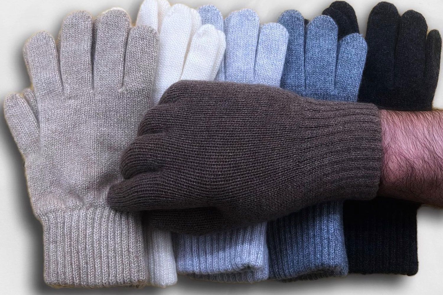 Assortimento di guanti invernali lavorati a maglia nei colori grigio, bianco, blu, nero e rosa, disposti in una pila.
