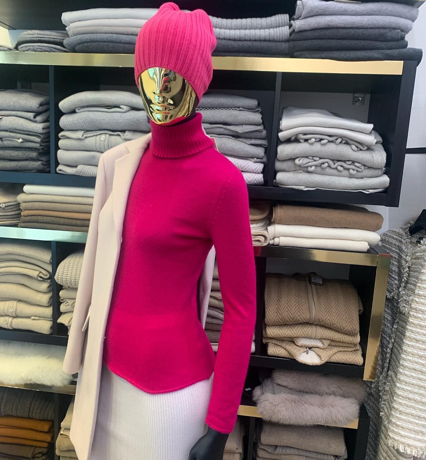 Manichino con dolcevita rosa acceso e pantaloni bianchi, con berretto rosa in testa, in un negozio di abbigliamento.