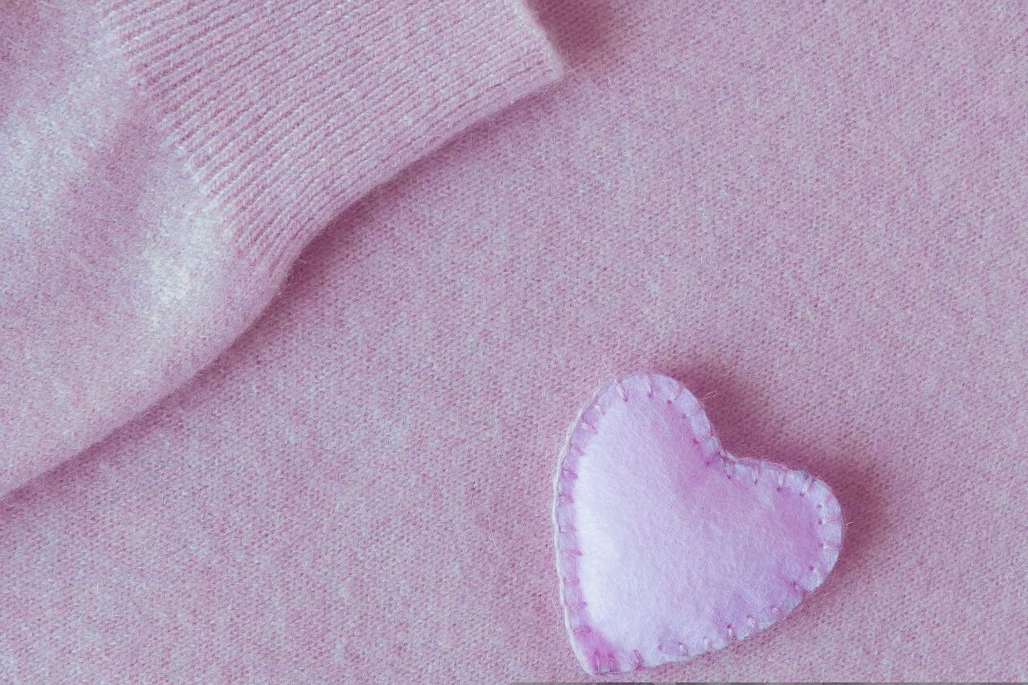 Toppa in tessuto rosa a forma di cuore su uno sfondo rosa tenue con stoffa piegata in un angolo.