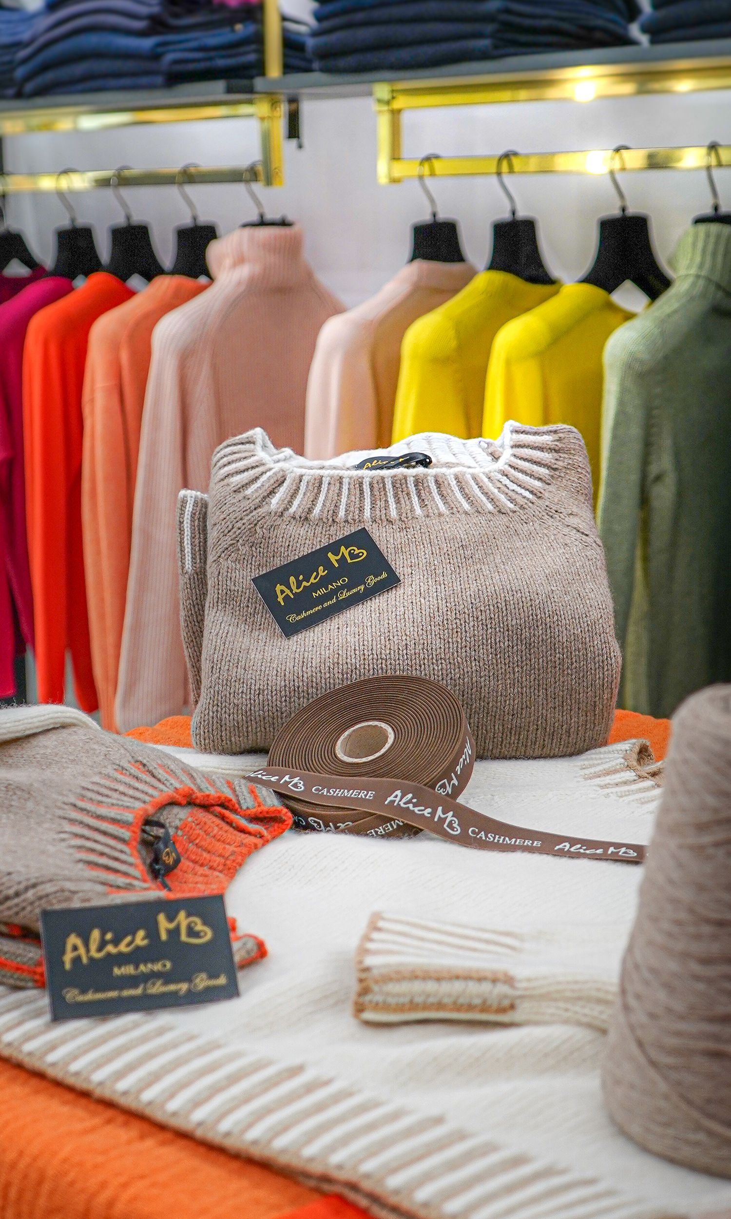 Maglioni colorati e accessori in maglia esposti su uno stand e un tavolo in una boutique di abbigliamento.