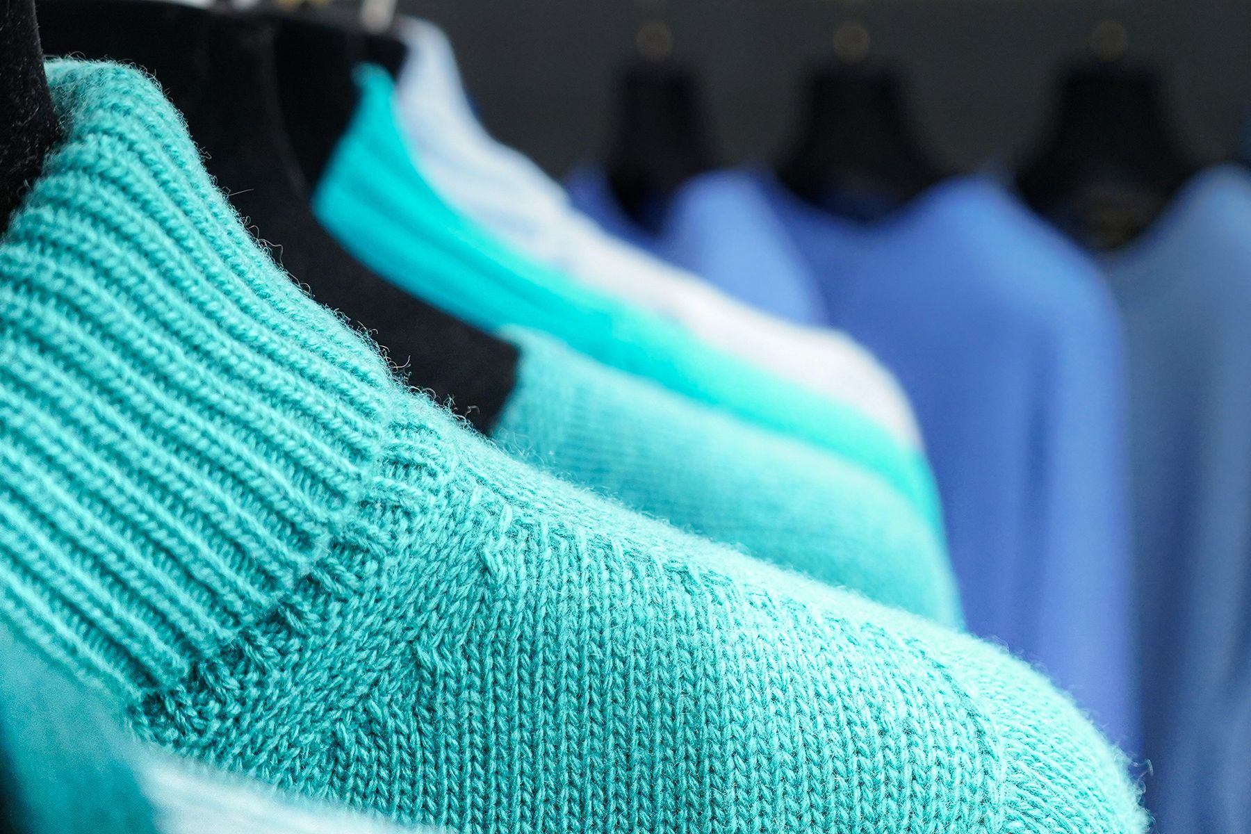 Maglione color verde acqua appeso a uno stendino, con sullo sfondo abiti blu sfocati.