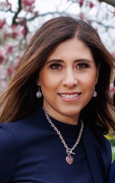 A woman wearing a necklace and earrings is smiling for the camera.
