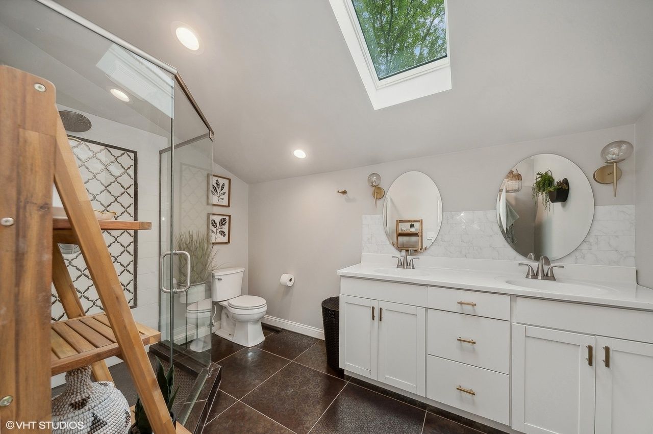 A bathroom with a toilet , sink , mirror and skylight north shore il