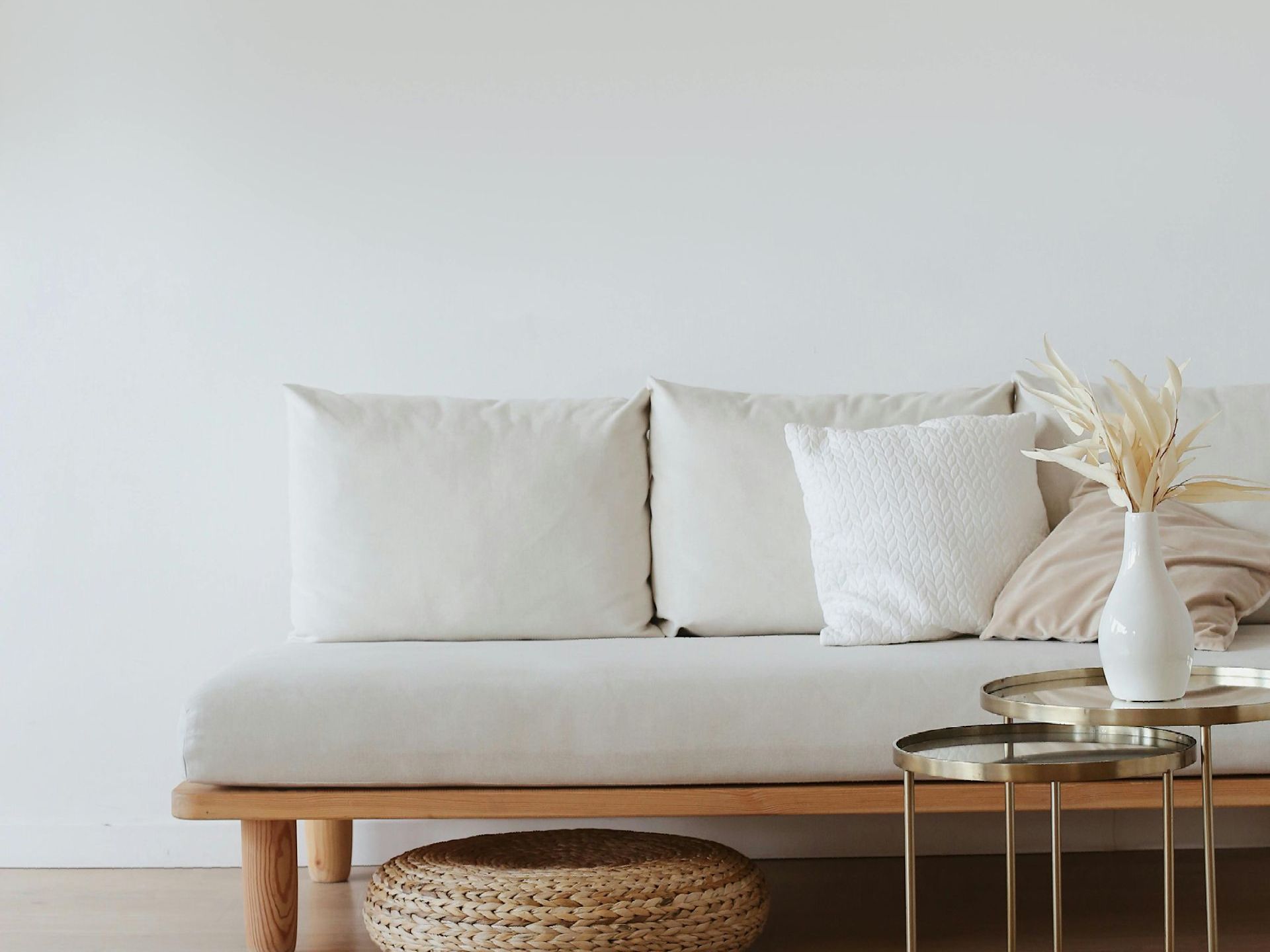 A couch with white pillows and a vase of dried flowers on it in a living room.