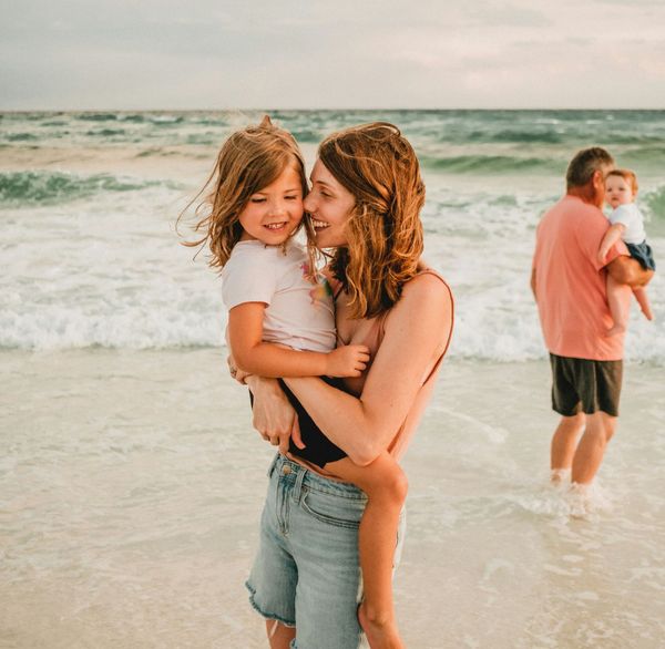 A woman is holding a little girl on the beach.